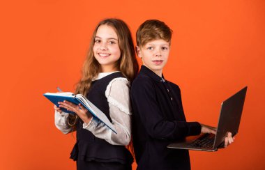 İlkokul öğrencileri. Küçük öğrenciler kitabı ve dizüstü bilgisayarı kahverengi arka planda tutarlar. Okulda küçük öğrenciler okuyor. Zeki öğrenciler ya da okul çocukları. E-öğrenme ve çevrimiçi eğitim. Yeni teknoloji