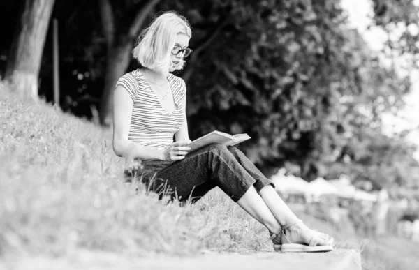 Література для літніх канікул. Дівчина розслабляється на березі річки після робочого дня. Розслабтеся і захоплюйтеся. Літня відпустка. Студентський розумний ботанік сидить на зеленій траві і читає книгу. Жінка мріє про відпустку — стокове фото
