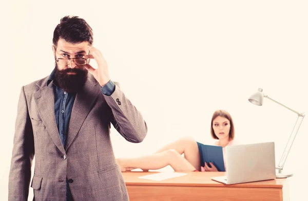 Smart and good looking guy. Smart man looking through glasses with sexy woman working in background. Bearded man in smart casual wear with coworker. Smart businessman and pretty secretary in office — Stock Photo, Image