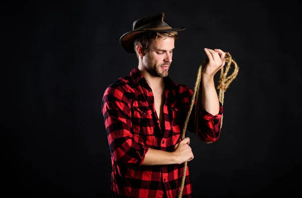 A vida ocidental. Homem unshaven cowboy fundo preto. Homem de chapéu segura corda. Ferramenta de laço de cowboy americano. Lasso é usado em rodeios como parte de eventos competitivos. Lasso pode ser amarrado ou embrulhado — Fotografia de Stock