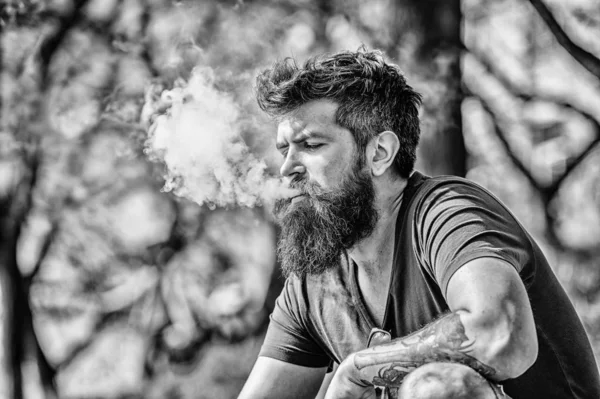 Man long beard relaxed with smoking habit. Man with beard and mustache breathe out smoke. White clouds of flavored smoke. Stress relief concept. Bearded man smoking vape. Smoking electronic cigarette