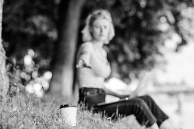 Kahve fincanı yakın çekim götürmek. Dizüstü bilgisayar defocused arka plan ile yeşil çim kadın işçi kahve fincanı. Temiz hava konseptinde kahve molası. Doğanın kafein gücü. Enerji şarjı ve ferahlığı