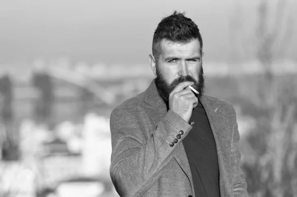 Smoking devices concept. Bearded hipster smoking outdoors. Device hide conceal smell of smoke. Handsome man smoke flying out of mouth. Cigarette tobacco harmful health influence. Smoking aesthetics