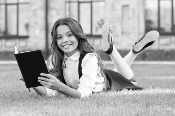 Tillgång till kunskap. Lektion i frisk luft. Söt liten barnbok utomhus. Lärobok. Litteratur för barn. Skolflickans skoluniform ligger på gräsmattan med favoritbok. Bokmaskskoncept — Stockfoto