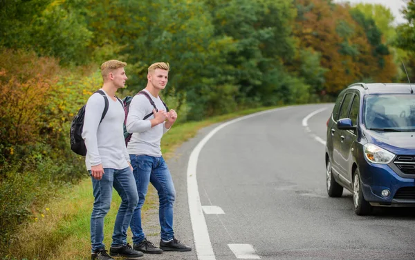 Hitchhiking gesture. Begin great adventure in your life with hitchhiking. Company friends travelers hitchhiking at road nature background. Travellers on their way. Friends hitchhikers travelling — Stock Photo, Image