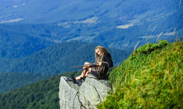 Aiming concept. Hunting season. Hunter mountains landscape background. Sexy warrior. Woman attractive long hair pretty face hold rifle for hunting. Amazon girl sit on cliff prepare gun for hunting — Stock Photo, Image