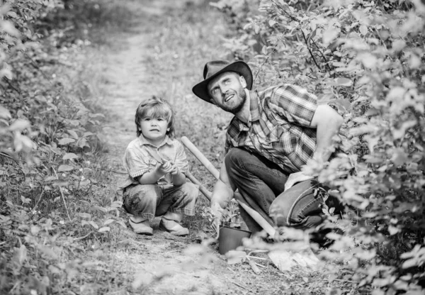 Öko-farm. kapa, pot és lapát. Kerti felszerelések. kisfiú gyermeke segít apja a gazdálkodásban. apja és fia cowboy kalapban a tanyán. boldog föld nap. Családi fa nursering. Hivatásos Kertész — Stock Fotó