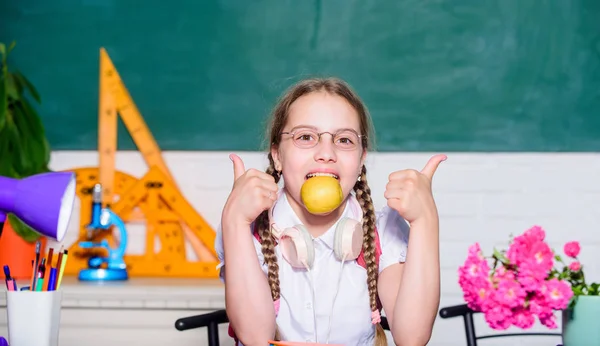 Školní životní koncept. Moderní dětství. Školní prázdniny. Svačinka mezi lekcemi. Školačka sedět stůl tabuli pozadí. Student na škole. Holka, co jí jablečný ovoce. Zdravý životní styl — Stock fotografie