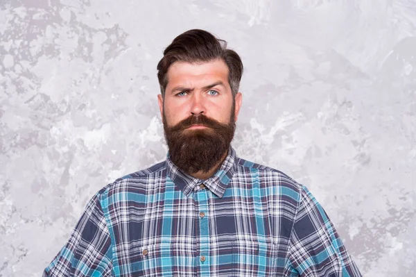 Masculine traits. Brutal bearded man concrete background. Serious man with beard and moustache. Confident hipster. Hairdresser in checkered shirt. Hipster style. Guy hipster outfit. Mature and trendy