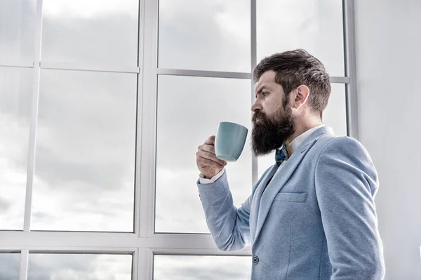 Man stand at window nervous about wedding. Life choices and expectations. But first coffee. His big day. Wedding morning concept. Wedding day. Groom bearded hipster man wear blue tuxedo and bow tie