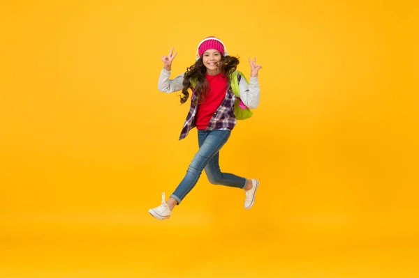 Finally vacation. Little girl listen music in headphones. Small schoolgirl running to school. Hurry up. Towards school knowledge. Run and jump. Kid captured in mid air. School happiness and joy