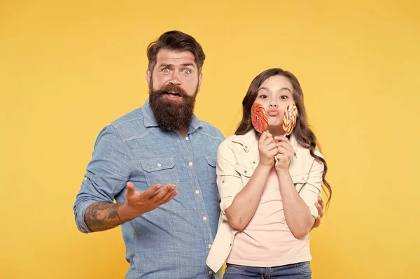 Sharing sweets with dearest people. Girl child and dad hold colorful lollipops. Sweet dessert. Bearded hipster good daddy for adorable daughter. Daughter and father eat sweet candies. Sweet childhood