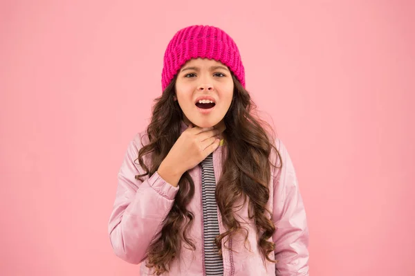목을 조르고. 추운 기후. 어린 소녀가 아픈 분홍색 배경을 가지고 있다. 애송이 퍼 플 재킷에 뜨개질 모자. 겨울 감기. 건강 관리. 기분이 안 좋아. 의학적 치료. 독감 치료제. 독감의 계절 — 스톡 사진