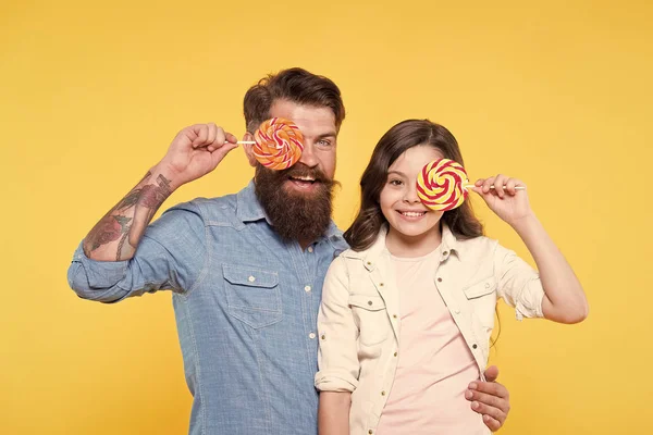 Lieve kindertijd. Meisje kind en papa houden kleurrijke lollies. Zoete dessert. Bearded hipster goede papa voor schattige dochter. Snoep en traktaties concept. Dochter en vader eten zoete snoepjes — Stockfoto