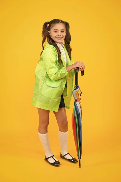 Mode et confortable. Joyeux écolier avec look d'automne à la mode sur fond jaune. Petite fille souriante en imperméable à la mode avec canne à parapluie. S'amuser avec des couleurs à la mode — Photo