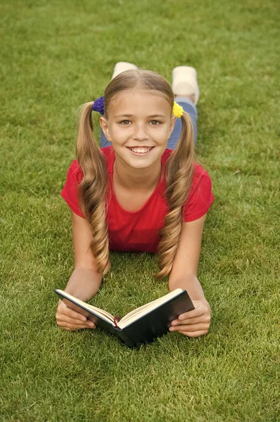 À l'école. Des histoires intéressantes pour les enfants. Étudier avec plaisir. C'est l'heure des grandes histoires. Petit enfant lisant un livre à l'extérieur. Écolière lire des histoires tout en relaxant pelouse verte. élève mignon profiter de la lecture — Photo