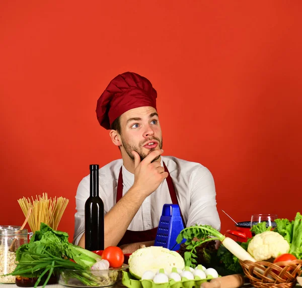 Шеф-повар с заботливым лицом сидит за столом с овощами — стоковое фото