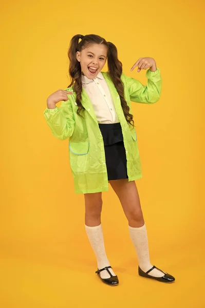 Soy guay. Niño pequeño y feliz señalando con los dedos sobre fondo amarillo. Pequeño escolar en el día de otoño. Niña pequeña de vuelta a la escuela con tiempo lluvioso. Adorable niño pequeño en verde raingear —  Fotos de Stock