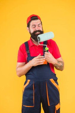 Boya aletini tamir et. Patenli neşeli sakallı işçi. Hipster sanatçı dekoratörü sarı duvar. İş üniformalı ereksiyon asistanı. Mühendis tasarımcı duvarı boyamaya hazır. onarım kavramı