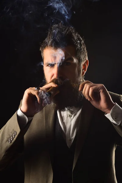 Businessman with strict face smokes cuban cigar.