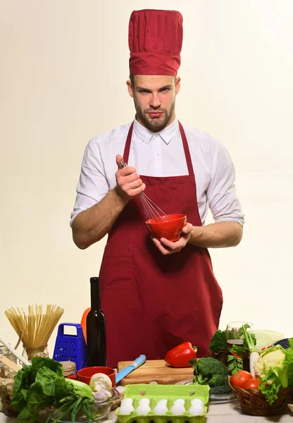 Chef en uniforme de borgoña agita los ingredientes con batidor . — Foto de Stock