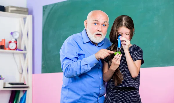 Wetenschapslab. klein meisje verkennen fruit slice. school. Microscopie. Analyse en synthese. kennis van de wereld uit te breiden. biologisch monster. volwassen leraar kijken door vergrootglas buis op kalk — Stockfoto