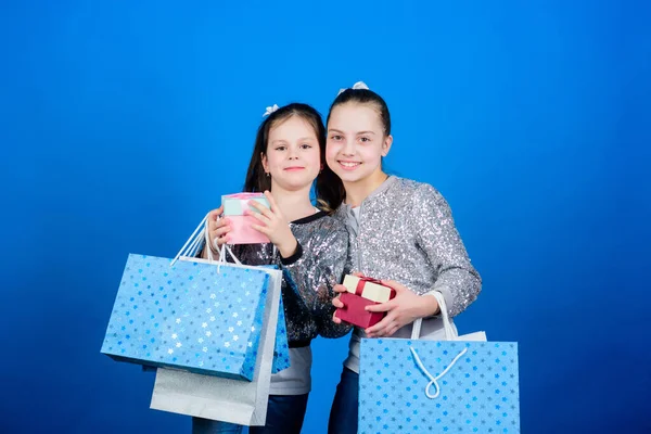 Meisjes zussen vrienden met boodschappentassen blauwe achtergrond. Winkelen en kopen. Zwarte vrijdag. Verkoop en korting. Kinderen pakketjes. Winkeldag. Kindermode. Elk product geleverd aan u — Stockfoto