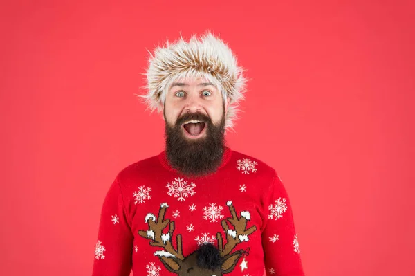 Oslava zimních prázdnin. Chladné počasí pro muže. Šťastný nový rok. vousatý muž se usmívá na červeném pozadí. legrační muž s vousy v pleteném svetru. překvapený hipster připraven na vánoční večírek — Stock fotografie