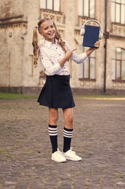 Dinleme okul kitabı. Bilgi bu şekilde daha iyi asimile. Sesli kitap konsepti. Öğrenme için dijital teknolojiler. E-öğrenme ve modern yöntemler. Kız sevimli kız öğrenci kitap ve kulaklık tutun
