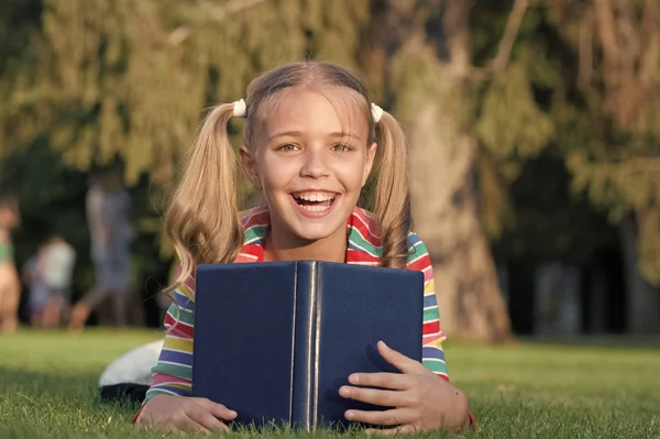 Moje vzdělání pochází z encyklopedie. Šťastná holčička čte encyklopedii na zelené trávě. Rozkošný dětský úsměv s knihou encyklopedie. Encyklopedie a informace — Stock fotografie