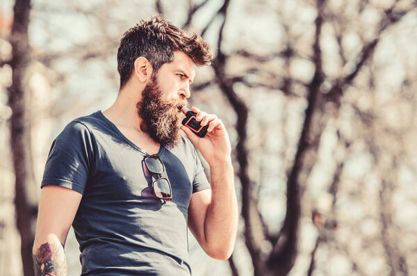 Бородатый жестокий мужчина курит электронную сигарету. мужчина курит электронную сигарету. Хипстерский человек держит ваппинговый прибор. Безопасность и зависимость от здоровья. Вдыхаю пар. Зрелый хипстер с бородой. Вапинг-концепция
