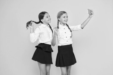 Bir selfie daha. Mutlu öğrenciler sarı arka planda akıllı telefonla selfie çekiyorlar. Cep telefonuyla selfie kameraya gülümseyen küçük kızlar. 1 Eylül'de selfie oturumu keyfi