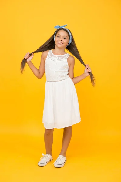 Krása účes. Šťastná dívka nosit dlouhé vlasy žluté pozadí. Malé dítě drží hnědé vlasy. Nádherný účes. Kosmetický kadeřnictví. Módní účes, stylový vzhled — Stock fotografie