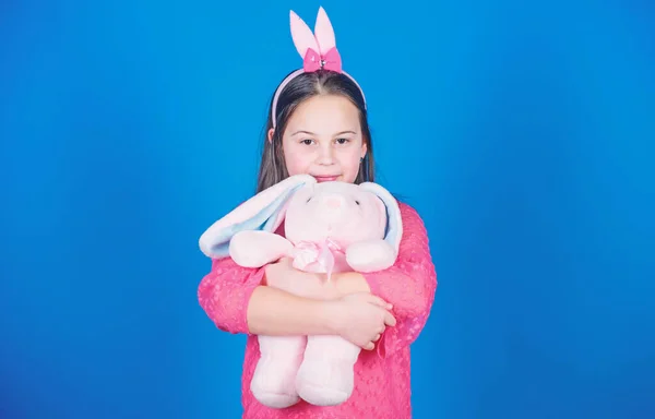 Haben Ostern gesegnet. Bunny Girl mit niedlichem Spielzeug auf blauem Hintergrund. Kinder lächelnd spielen Hasenspielzeug. glückliche Kindheit. Einstimmung auf Ostern. Hasenohren als Accessoire. schönes verspieltes Hasenkind umarmt Kuscheltier — Stockfoto