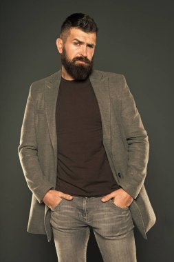 Sakallı ve barbar. Sakallı adam gri arka planda kollarını cebinde tutuyor. Sıradan tarzda sakallı hippi. Vahşi traşsız adam sakallı yüzüne bıyık ve sakal takıyor.