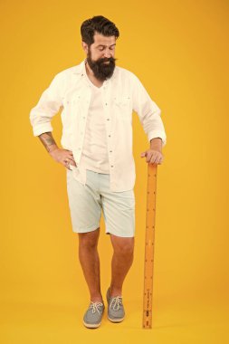 Bir çizgiyi ölçüyor. Adam okula geri döndü. Öğretmen adam sarı arka planda metrik cetvel tutuyor. Matematik ve geometri dersine hazırlanan acımasız adam. Büyük ölçüm aleti ile sakallı adam