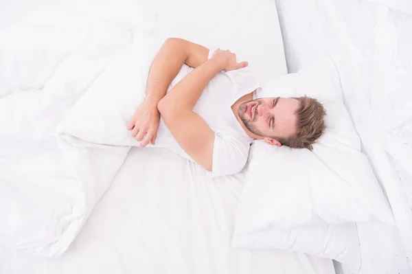 Проблемы со сном могут привести к головной боли утром. Головные боли мигрени. Красивый мужчина расслабляется в постели. Храп может увеличить риск головной боли. Обычный симптом апноэ во сне. Причины головной боли ранним утром — стоковое фото