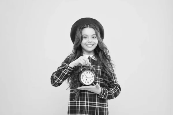 Retro es atemporal. Feliz niño pequeño sosteniendo reloj retro sobre fondo amarillo. Niña sonriendo con reloj de diseño retro. Adorbale niño con reloj vintage en estilo retro — Foto de Stock