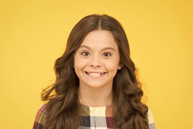 Çocuğu mutlu eden eğitim. Sarı arka plandaki mutlu küçük kız. Uzun esmer saçlı küçük çocuk gülümsemesi. Mutlu bir çocukluk. Okul zamanı.