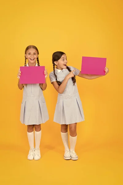 Delivering fresh information. Announcement and promotion. Schoolgirls cheerful pupils informing you. Girls school uniform hold posters. Back to school. School girls hold blank paper copy space