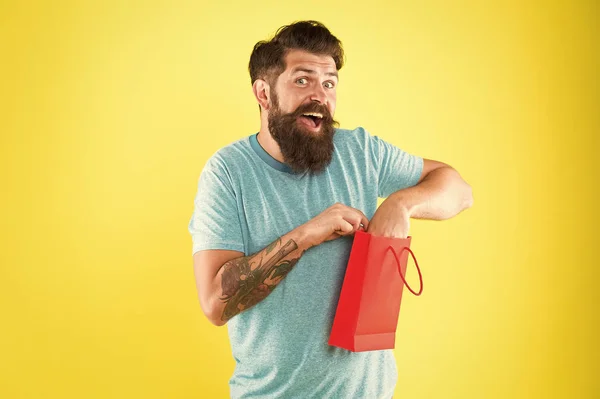 Счастливый хипстер держит бумажный пакет. Бородатый мужчина улыбается при покупке. Импульсная покупка. Концепция покупок. Магазин в торговом центре. Купить товар. Аспекты могут влиять на поведение клиентов при принятии решений — стоковое фото