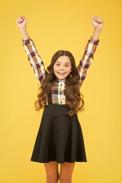 Celebrate the childhood. Happy girl with raised hands yellow background. Small girl back to school. Girl celebrating school holidays. Cute girl with long hair smile in formal wear — Stock Photo, Image