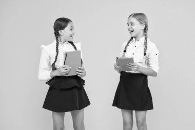 Gerçekten okumaya izin verir. Sarı arka planda kütüphane kitapları tutan sevimli küçük kızlar. Sevimli küçük çocuklar ilkokulda okumayı öğreniyor. Okuyun ve elde edin