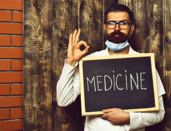 Brutalny, biały lekarz trzymający deskę z napisem Medycyna na brązowym drewnianym tle studia vintage — Zdjęcie stockowe
