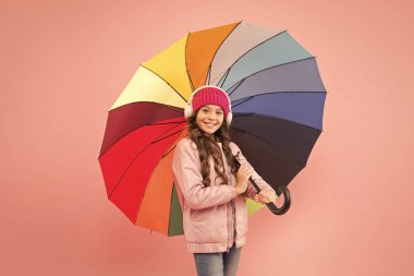 Yağmur yağarsa. Paltolu mutlu küçük çocuk yağmura karşı renkli şemsiye tutuyor. Moda aksesuarlı şirin küçük kız müzik dinliyor. Islak yağmur havasında onu kuru tut. Yağmur sağanağı için harika.