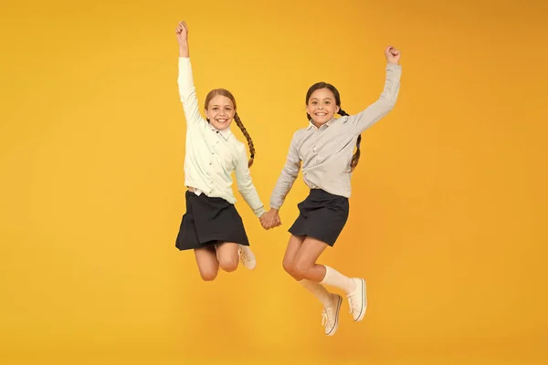 Cuties no ar. Crianças ativas pulando alto no fundo amarelo. Meninas felizes desfrutando de estilo de vida ativo. Amigos da escola se divertindo juntos. Geração activa. Ativo e energético — Fotografia de Stock