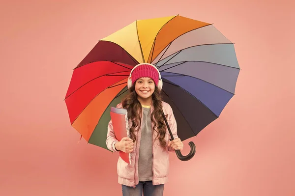 Für Regenwetter konzipiert. kleine Schulmädchen halten bunten Regenschirm auf rosa Hintergrund. Im Herbst geht das kleine Kind wieder zur Schule. entzückendes Kind mit Kopfhörern geht an einem regnerischen Tag zur Schule. die beste Schule — Stockfoto