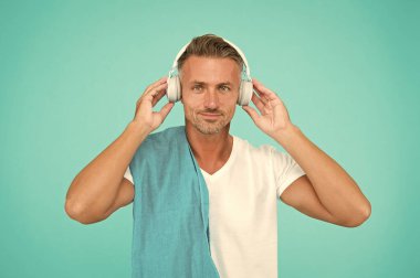 Müzikle alıştırma yapıyorum. Yakışıklı adam mavi arka planda müzikten hoşlanıyor. Atletik adam kulaklıkla müzik dinliyor. Müzik dinlemek egzersizini geliştirir. Spor salonunda eğitim.