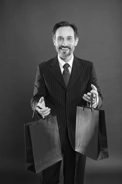 Pomáhám hospodárnosti, hodně nakupuju. Šťastný zákazník červené pozadí. Podnikatel drží nákupní tašky. Starší muž rád nakupuje. Výprodej. Nákupní dárky. Černý pátek. Dobrý den na nákupy — Stock fotografie