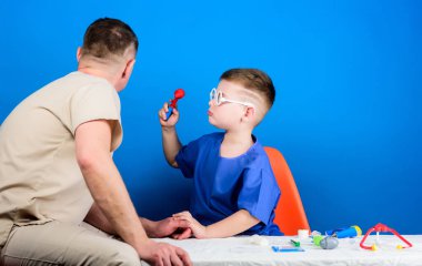 Tıp konsepti. Küçük doktor, masada tıbbi aletlerle oturuyor. Hastalık tedavisi. Baba ve oğul tıp hanedanlığı. Tıbbi muayene. Tatlı çocuk ve babası doktor. Hastane çalışanı. Sağlık hizmetleri